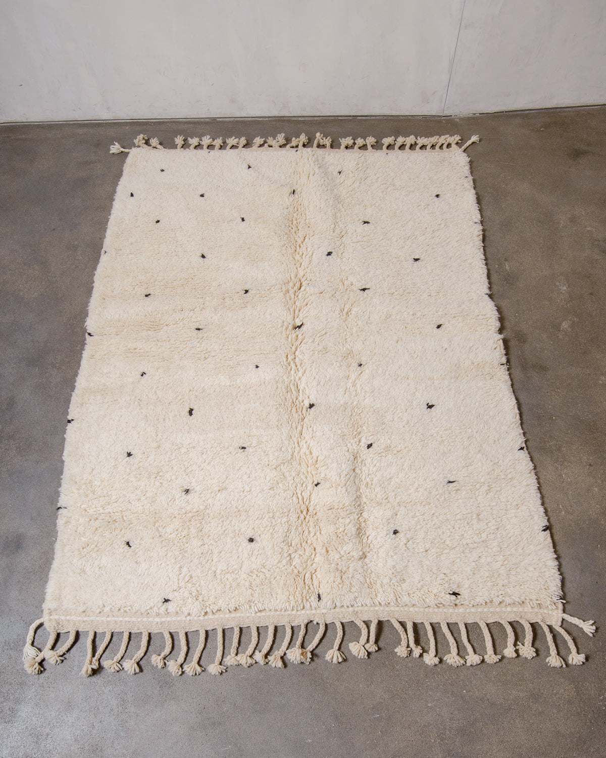 Berberlin Beniourain rug in cream wool with black dots laying on concrete floor.